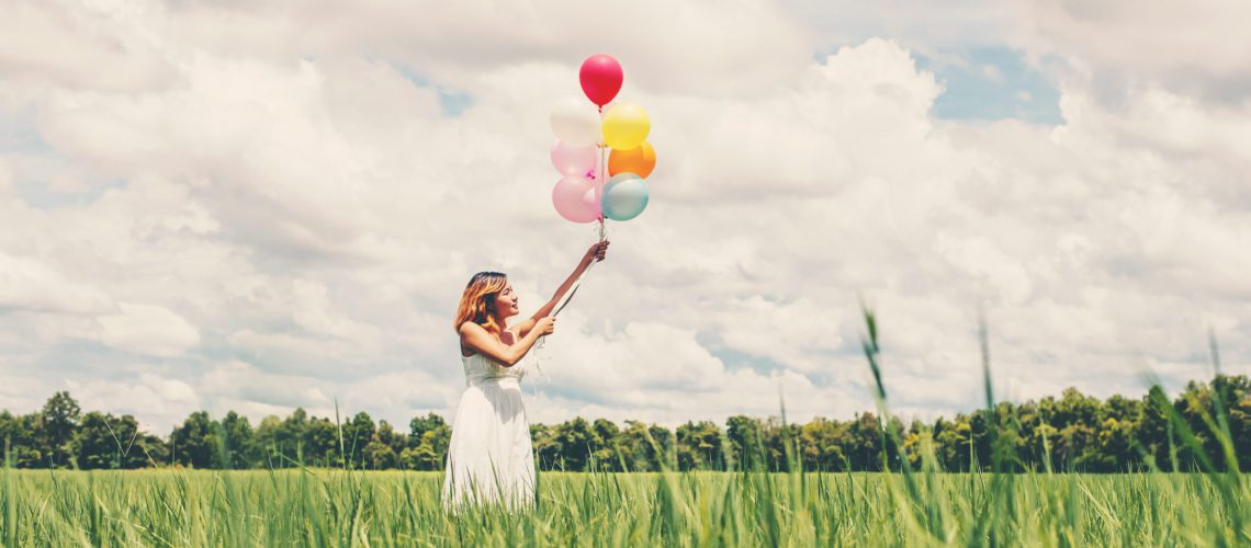 Happy young beautiful woman holding balloons in the grass field enjoy with fresh air.